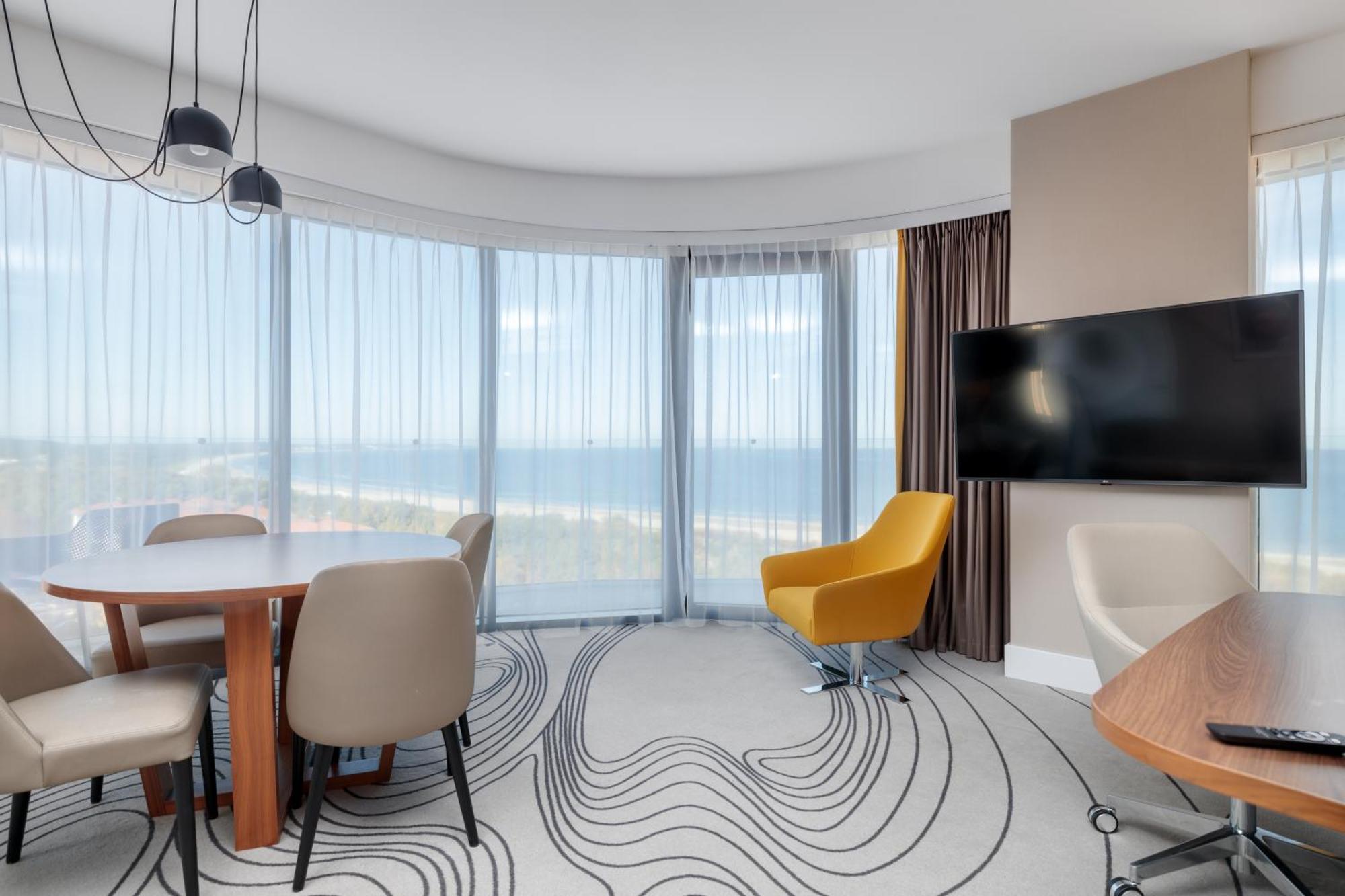 Radisson Blu Resort ชวีโนวิชแจ ภายนอก รูปภาพ The image shows a modern hotel room or suite with a bright, airy atmosphere. There are large windows that allow natural light to fill the space, providing a view of the ocean. The decor includes a round dining table with several chairs, and a stylish