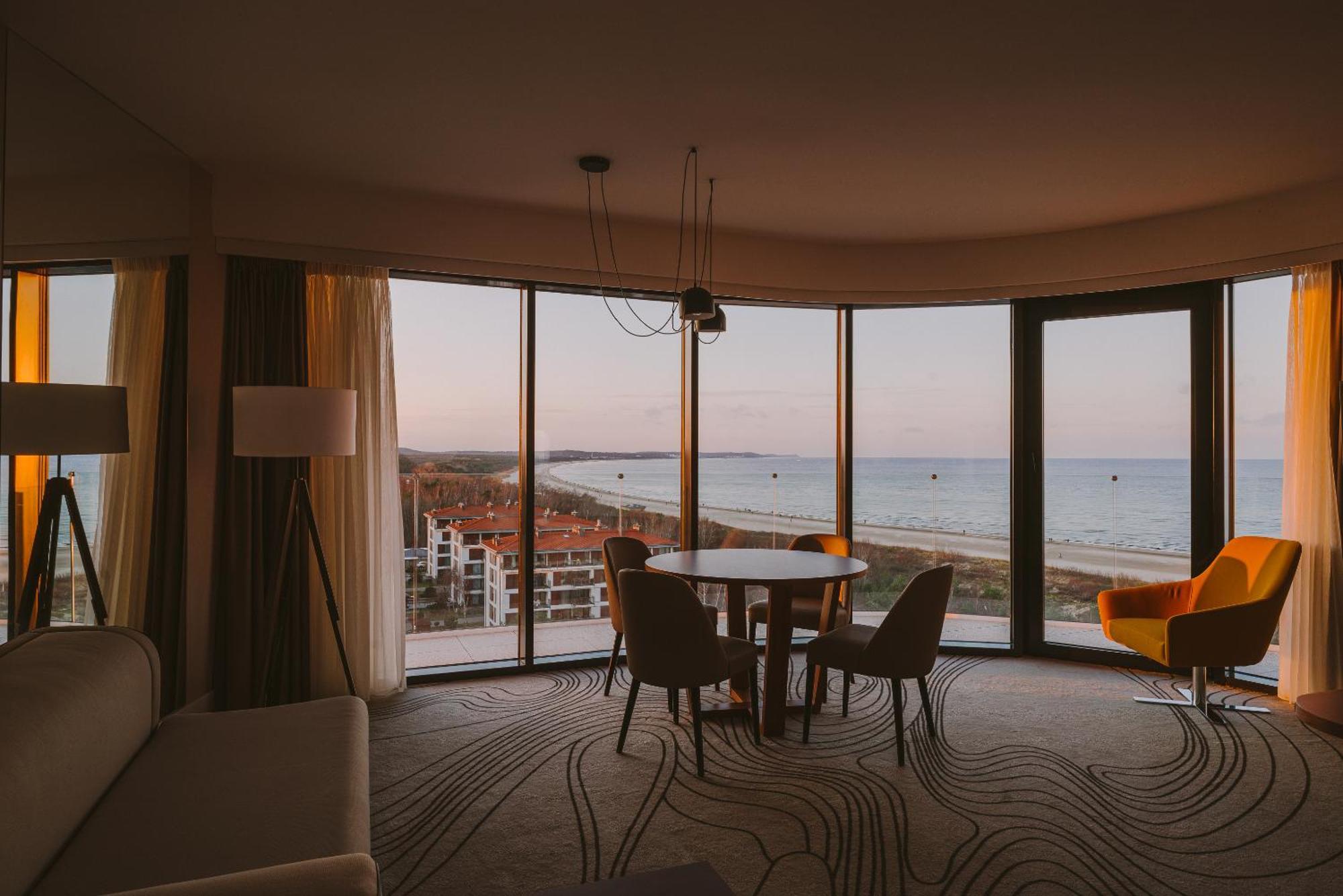 Radisson Blu Resort ชวีโนวิชแจ ภายนอก รูปภาพ The photo shows a modern and stylish interior of a room featuring large windows that provide a view of the beach and ocean. The room is furnished with a round table and chairs, along with a cozy sofa and a bright yellow armchair. The decor has a cont