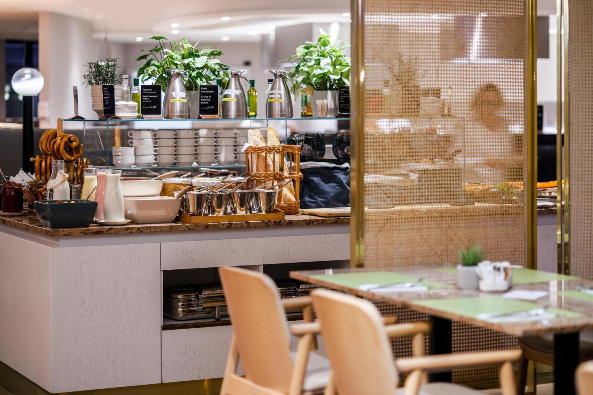 Radisson Blu Resort ชวีโนวิชแจ ภายนอก รูปภาพ The photo shows a modern café or dining area. In the foreground, there are wooden chairs and tables set up for dining. In the background, there is a display counter with various items, including plants in pots, containers, and possibly dishes or uten