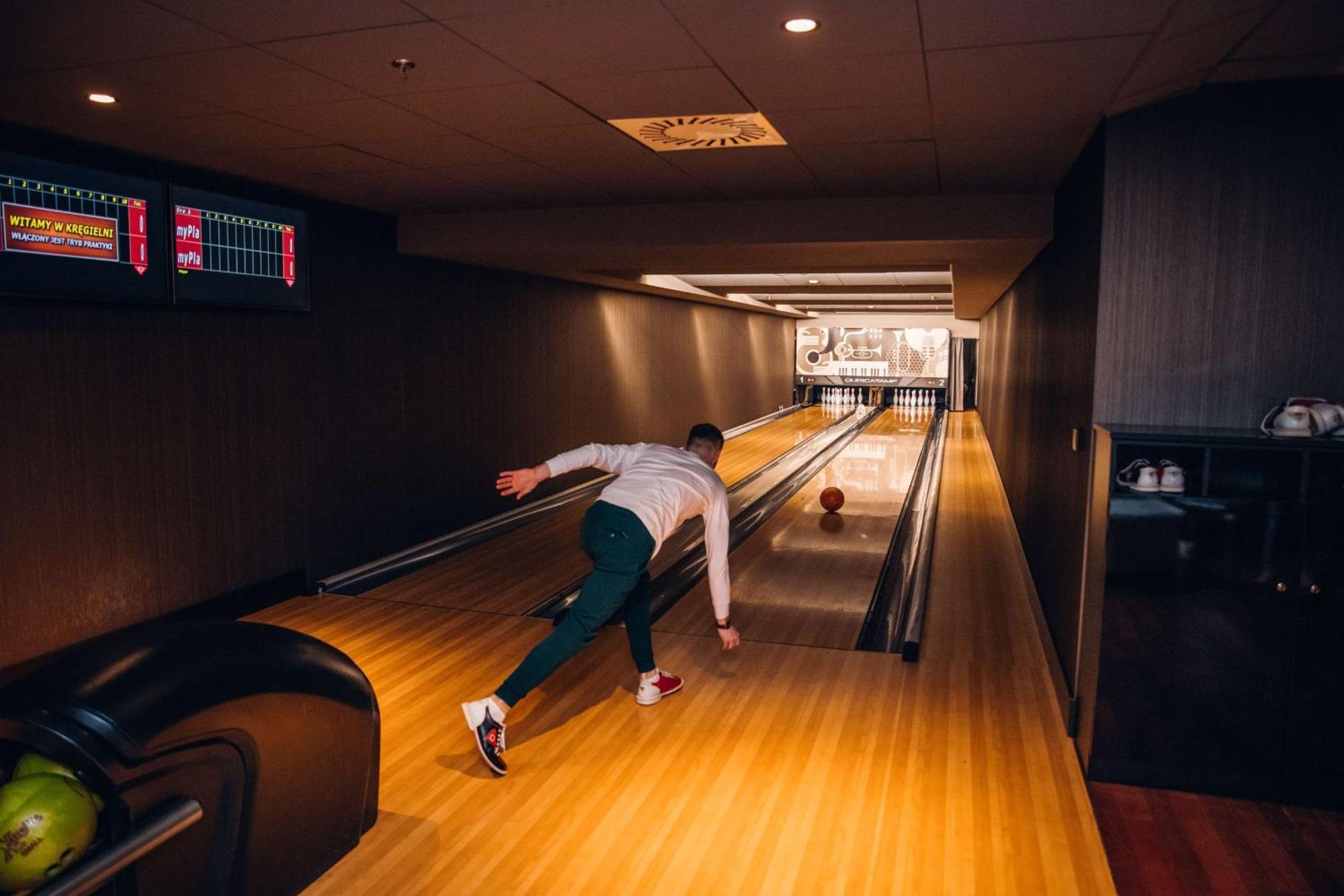 Radisson Blu Resort ชวีโนวิชแจ ภายนอก รูปภาพ The photo shows a bowling alley. In the foreground, a person is throwing a bowling ball down the lane. They are wearing a white top and green pants, with red and white shoes. The bowling lane is made of polished wood, and at the end of the lane, ther