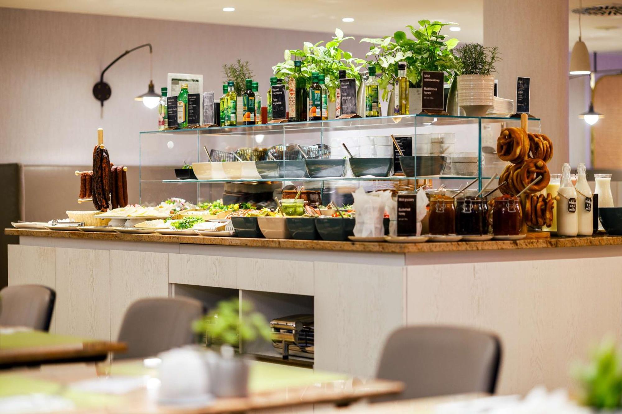 Radisson Blu Resort ชวีโนวิชแจ ภายนอก รูปภาพ The photo shows a well-organized buffet display in a restaurant setting. There is a glass counter filled with various dishes. On the upper shelf, there are several bottles of oil and herbs, indicating a focus on fresh and healthy ingredients. Below t