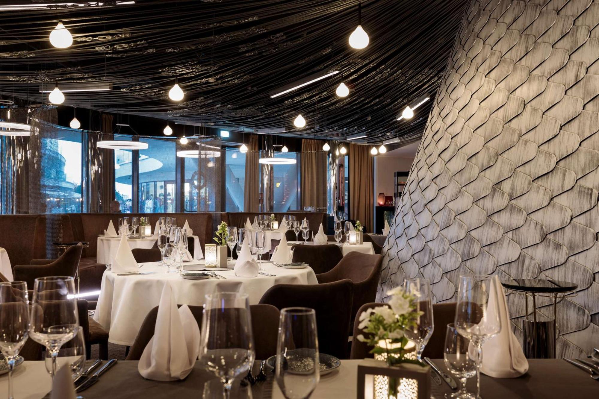 Radisson Blu Resort ชวีโนวิชแจ ภายนอก รูปภาพ The photo shows a stylish restaurant interior. The dining area features elegantly set tables with white tablecloths, glassware, and folded napkins. There are decorative elements like small floral arrangements on the tables. The ceiling is adorned wit