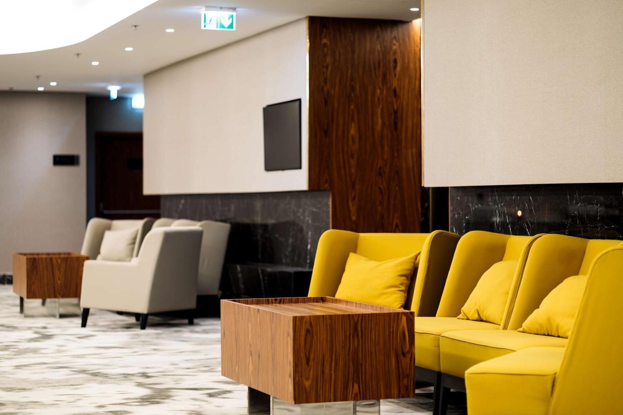 Radisson Blu Resort ชวีโนวิชแจ ภายนอก รูปภาพ The photo depicts a modern lounge or waiting area with stylish seating. On the left, there are soft gray armchairs arranged around a wooden coffee table. In the center, there are yellow chairs with plush cushions, contributing a vibrant contrast to t