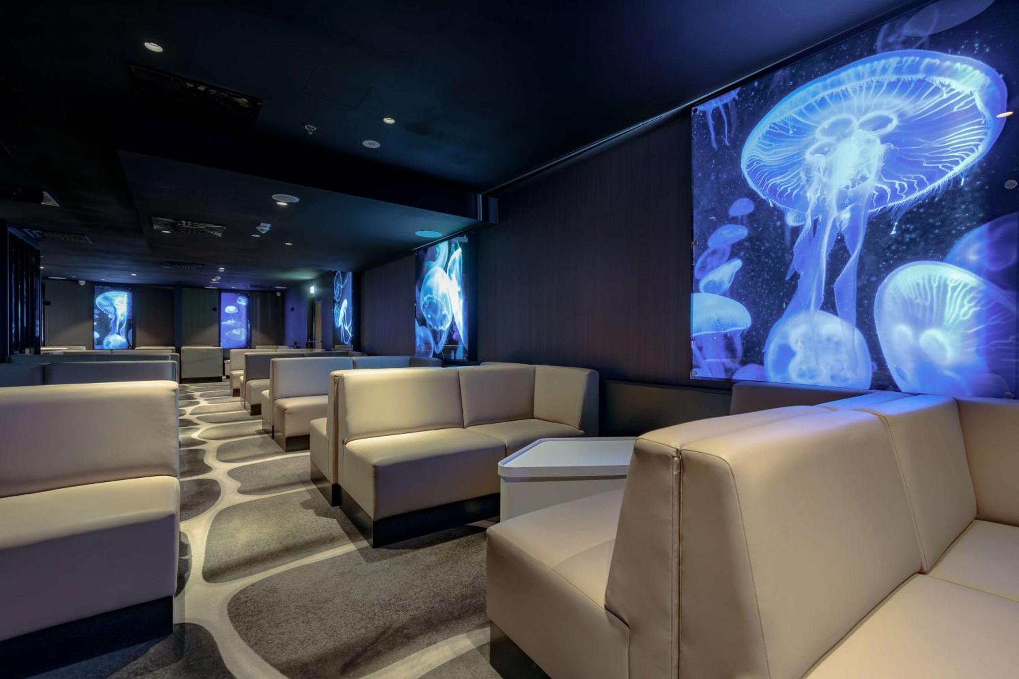 Radisson Blu Resort ชวีโนวิชแจ ภายนอก รูปภาพ The photo shows a modern lounge space with a sleek design. The area features light-colored, upholstered seating arranged in an open layout. The walls are decorated with large, vibrant images of jellyfish illuminated in blue, creating a calming underw