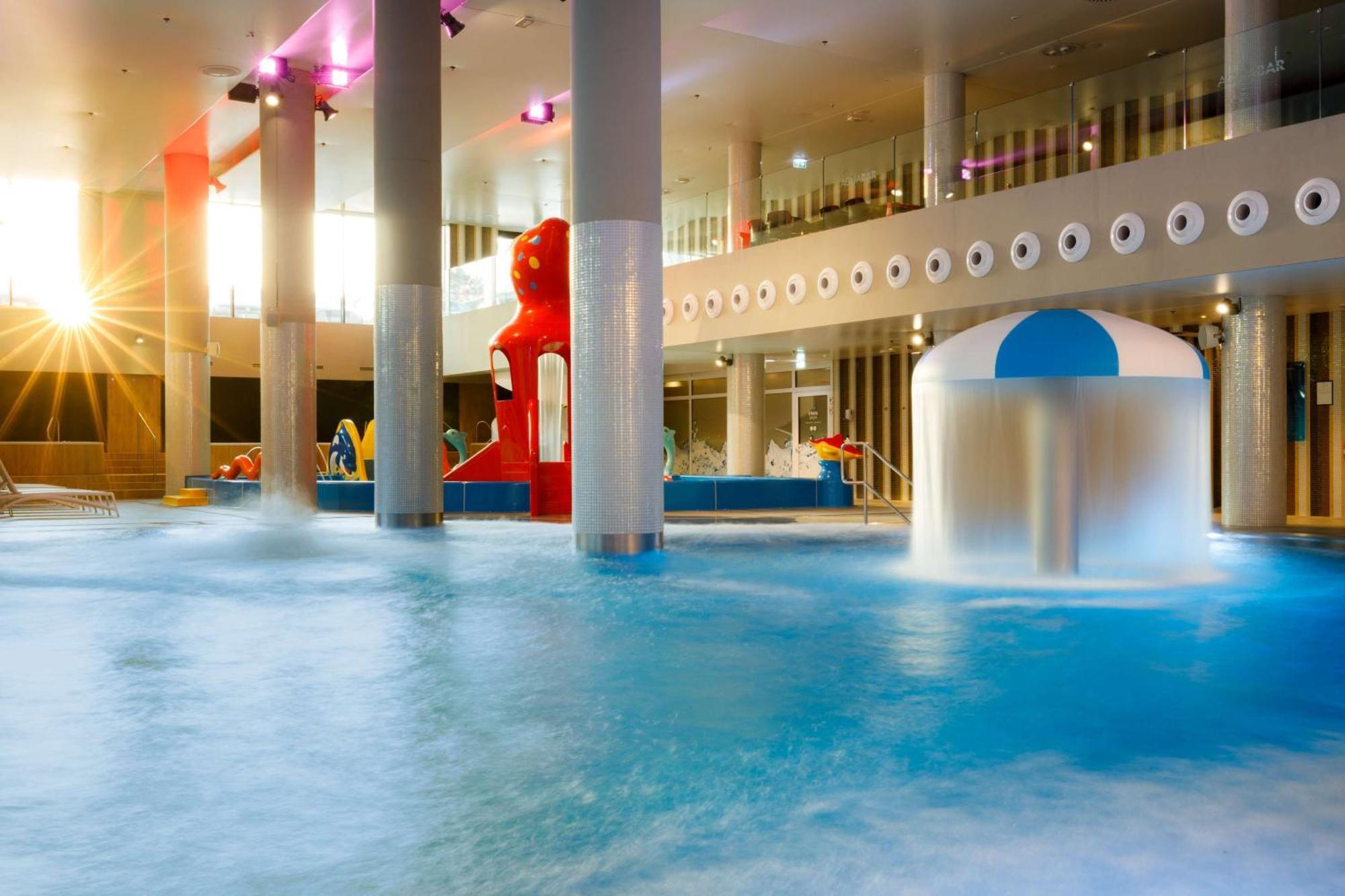 Radisson Blu Resort ชวีโนวิชแจ ภายนอก รูปภาพ The photo shows an indoor water park or pool area. There is a large body of water with playful features, including a water slide shaped like a red bear and a smaller structure with a blue and white canopy. The lighting is bright, suggesting a sunny a