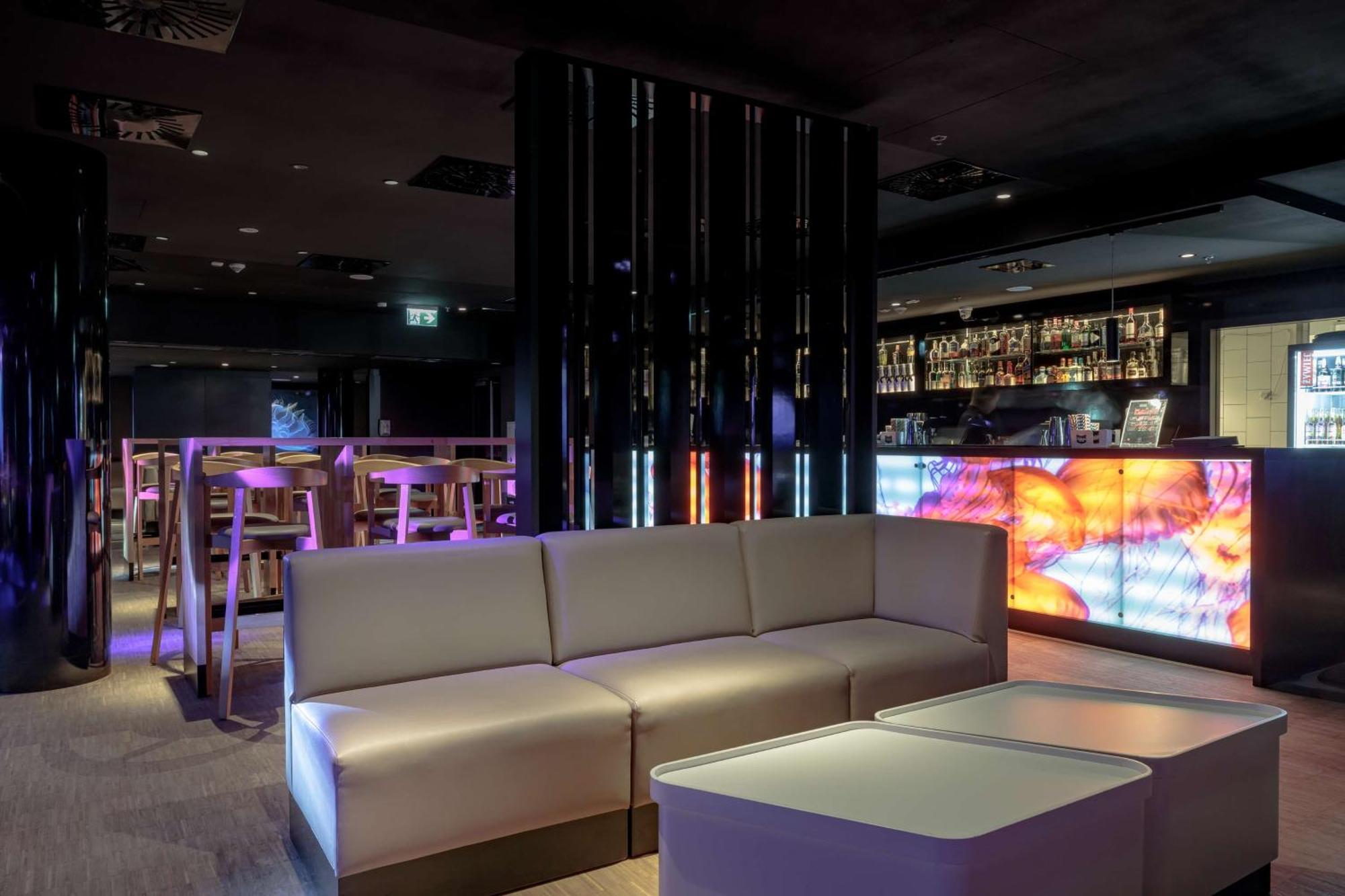 Radisson Blu Resort ชวีโนวิชแจ ภายนอก รูปภาพ The photo depicts a modern interior space, possibly a lounge or bar. There are sleek, minimalistic furniture pieces, including a large, curved sofa and contemporary coffee tables. The lighting is dim, with a blend of colorful ambient lights illuminat