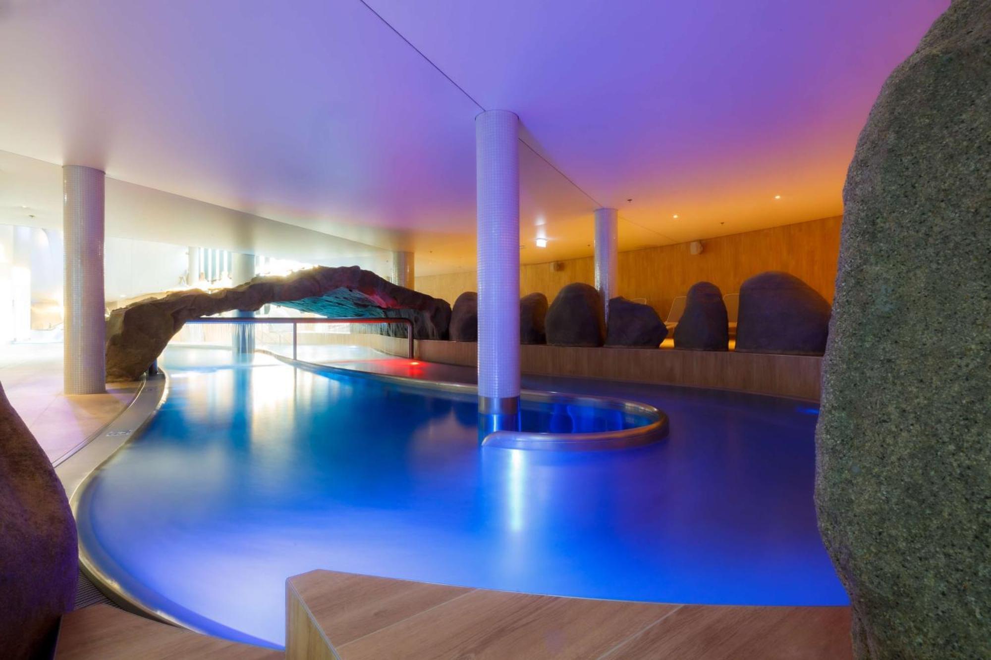 Radisson Blu Resort ชวีโนวิชแจ ภายนอก รูปภาพ The photo showcases an elegant indoor swimming pool area. The pool has a flowing, organic shape and is illuminated with soft blue and purple lighting, creating a calming ambiance. Surrounding the pool are smooth, natural-looking stones and wooden ele
