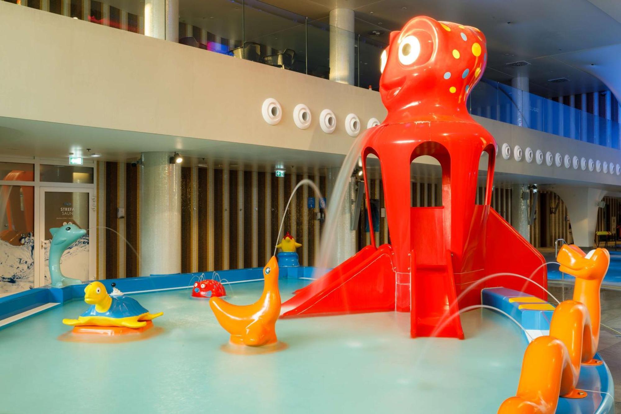 Radisson Blu Resort ชวีโนวิชแจ ภายนอก รูปภาพ The photo shows a colorful indoor splash pad or water play area designed for children. Central to the scene is a large, bright red octopus structure, which has water fountains spraying out. Surrounding it are various playful, colorful water animals, 